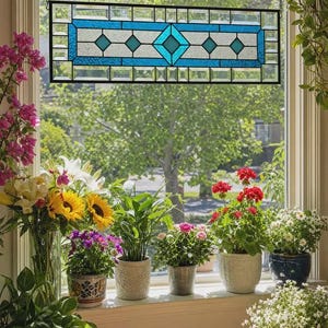 May include: A rectangular stained glass window hanging featuring a central blue diamond motif surrounded by white textured glass panels and a border of clear beveled glass pieces, all held together by a thin black metal frame and hanging chains.