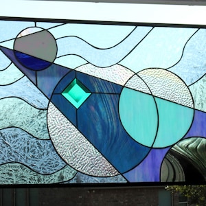 May include: A stained glass window with a geometric design featuring blue, green, and purple glass. The design includes circles, diamonds, and wavy lines.