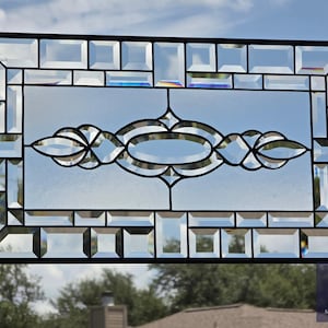 May include: A rectangular stained glass panel featuring a central oval motif with decorative flourishes, surrounded by a border of beveled glass rectangles. The piece is framed in black metal and includes hanging chains. The text SGCARTGLASS is visible.