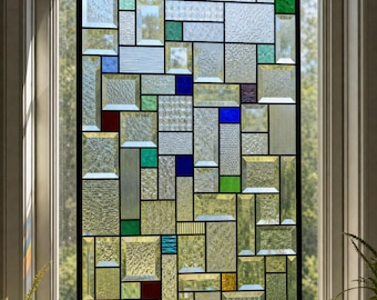 May include: A rectangular stained glass window hanging featuring a grid of clear, textured glass panels interspersed with small, vibrant squares of blue, red, green, and yellow glass, all held together by a thin black metal frame and hanging chains.