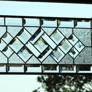 May include: A stained glass window panel with a geometric design featuring a diamond pattern. The glass is clear with a subtle iridescent sheen. The panel is framed in black metal.