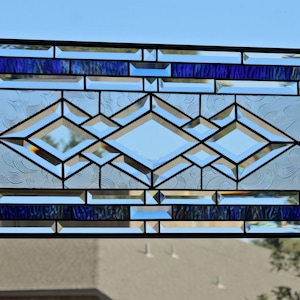 May include: A stained glass window with a geometric design featuring a series of diamonds in clear glass with a blue border. The window is framed in black metal.