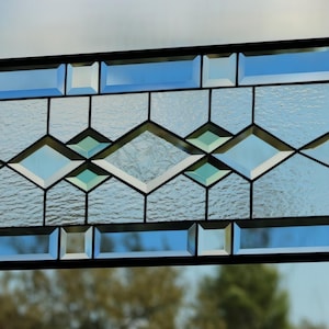 May include: A rectangular stained glass panel featuring a geometric pattern of clear beveled glass pieces. The design includes a central row of diamonds flanked by rectangular borders, all held together by a thin black metal frame structure.
