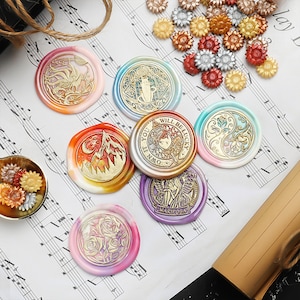 May include: Assortment of colorful wax seals with various designs, including a mountain, a cat, a flower, a fairy, and a rose. The seals are on a sheet of music.