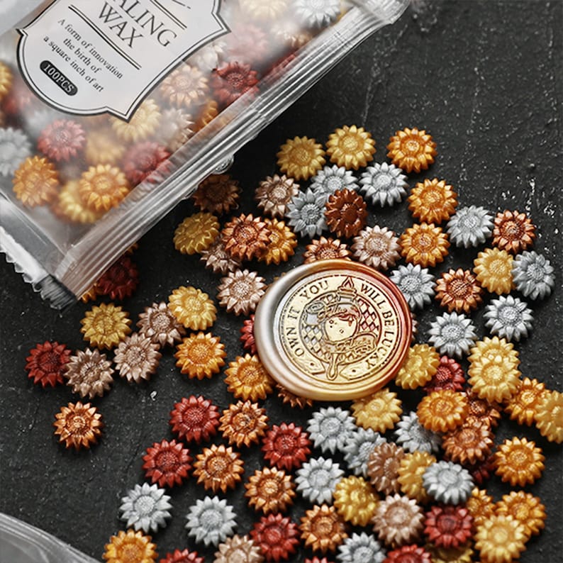 May include: A bag of 100 gold, silver, and copper sunflower-shaped wax seals. The wax seals are scattered on a dark surface. A gold wax seal with the text "Own it you! Will be lucky" is in the center of the image.