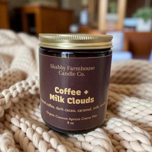 May include: A white ceramic mug with a black handle and the text "But First, Coffee" in a black, bold font. The mug is on a white surface.