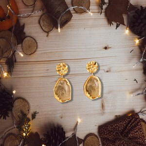 May include: A pair of gold-tone earrings with a textured, irregular-shaped stone pendant. The earrings have a modern, minimalist design.