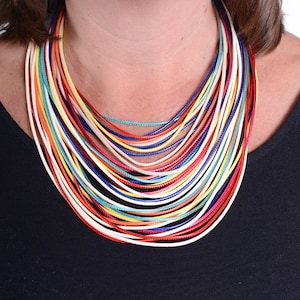 May include: A multi-coloured necklace made of thin cords in shades of red, orange, yellow, green, blue, and white. The necklace is layered and creates a bold statement.