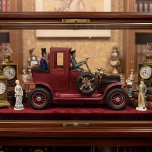 May include: A display case with a maroon and black antique car model, figurines, and clocks. The car has a spare tire and figures of people. The case also contains two antique clocks and several figurines. The display case is made of wood and glass.