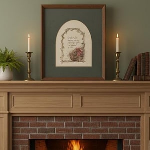 May include: A framed artwork featuring a nest with pink flowers and text, set against a green background. The artwork is displayed above a fireplace with lit candles in brass holders, a fern, and a stack of books. The overall aesthetic is warm and inviting.