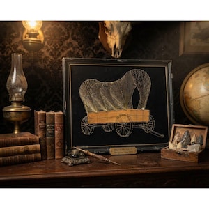 May include: A framed string art piece depicting a covered wagon on a black background. The artwork features a gold-toned plaque at the bottom center with the text PIONEER DAYS String Art, Circa 1972, encased in a simple black rectangular frame.
