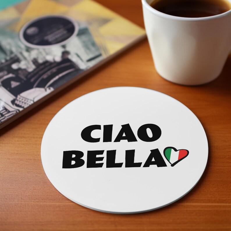 May include: White round coaster with the words "CIAO BELLA" in black, with a heart in the colors of the Italian flag. A white mug with coffee and a book are in the background.