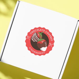 Könnte beinhalten: Weiße Box mit einem roten und weißen Aufkleber, auf dem "Chocolate Covered Strawberries" steht. Der Aufkleber zeigt zwei schokoladenüberzogene Erdbeeren.