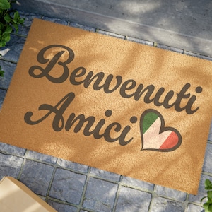 May include: A brown coir doormat with the text "Benvenuti Amici" in black cursive lettering and a heart-shaped Italian flag design.