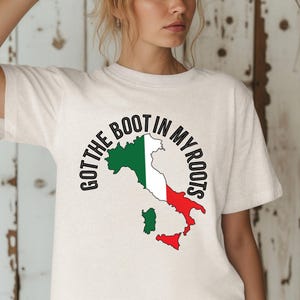 Könnte beinhalten: Cremefarbenes T-Shirt mit einer Grafik der italienischen Halbinsel in den Farben der italienischen Flagge: Grün, Weiß und Rot. Der Text "Got the Boot in My Roots" ist in Schwarz um die Grafik herum angeordnet.