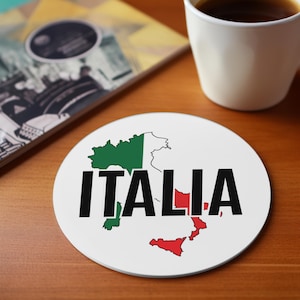 May include: White round coaster with a black outline of the Italian peninsula. The peninsula is colored in the colors of the Italian flag: green, white, and red. The word "ITALIA" is written in black letters across the center of the coaster.