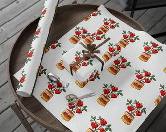 May include: White wrapping paper with a repeating pattern of red heart-shaped tomatoes growing from a jar. A wrapped gift with a brown ribbon and a roll of matching paper are on a wooden table. A pair of scissors and a spoon are also on the table.