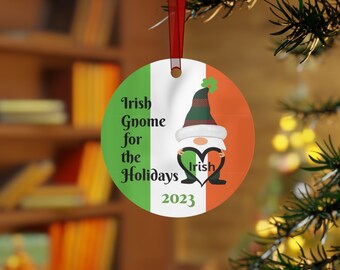 Könnte beinhalten: Runder Weihnachtsschmuck mit irischem Flaggen-Design. Der Schmuck zeigt einen Wichtel, der ein Herz mit dem Wort "Irish" hält. Der Text auf dem Schmuck lautet "Irish Gnome for the Holidays 2023". Ein rotes Band ist zum Aufhängen befestigt.