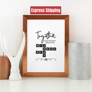 May include: A framed print with the word "Together" in elegant script, with the phrase "is our favorite place to be." Below, names are spelled out using Scrabble tiles. The frame is gold, and the print is displayed with decorative items.