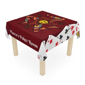 May include: A square table with a burgundy tablecloth featuring a Trinacria design and the text "Marco's Poker Room." The tablecloth has playing card edges. The table has four wooden legs.