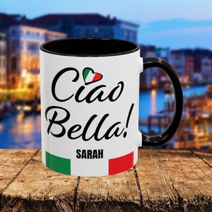 May include: White ceramic mug with a black rim and handle. The mug has a black and white graphic that says "Ciao Bella!" with a heart containing the Italian flag. The name "SARAH" is printed below the graphic.