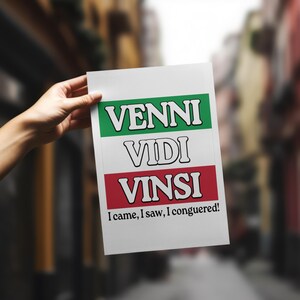 May include: A white sign with the Italian phrase "Venni Vidi VinsI" in black and red lettering. The phrase translates to "I came, I saw, I conquered!" in English.