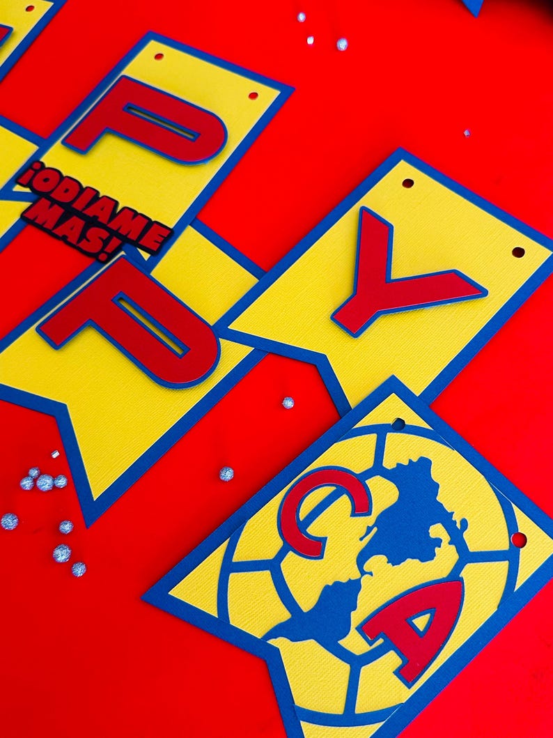 May include: A yellow and blue banner with the word "Happy" in red letters. The banner also includes a red and blue soccer ball with the letters "CA" in red. The text "&iexcl;ODIAME MAS!" is also on the banner.
