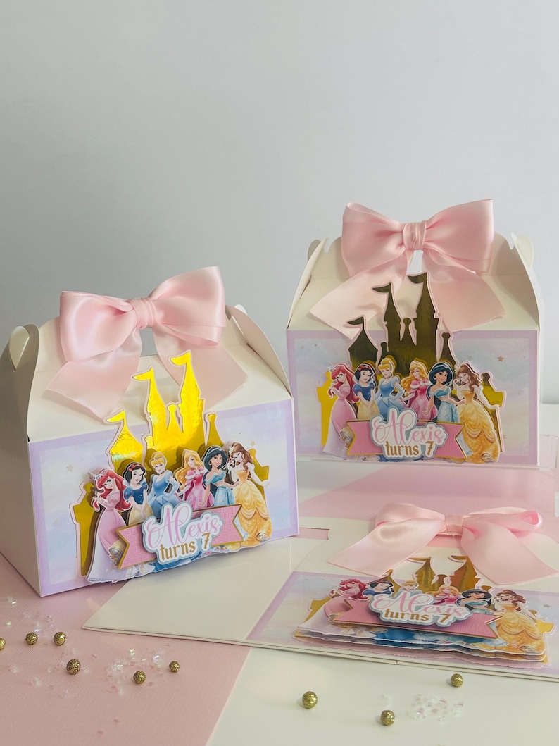 May include: A set of three princess-themed party favor boxes with pink bows. Each box features a gold castle and a group of Disney princesses. The text on the boxes reads "Alexis turns 7".