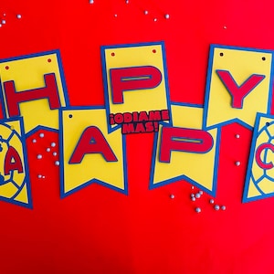 May include: A yellow and blue banner with red letters spelling "Happy" and a soccer ball with the letters "CA" on it. The banner also includes the text "&iexcl;ODIAMOS MAS!" in red letters.