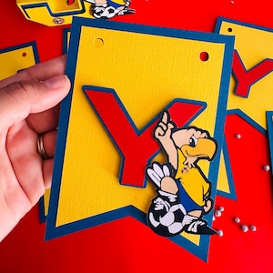 May include: A yellow and blue banner with the letter "Y" in red and a cartoon soccer player with a yellow jersey and blue shorts. The player is kicking a soccer ball.
