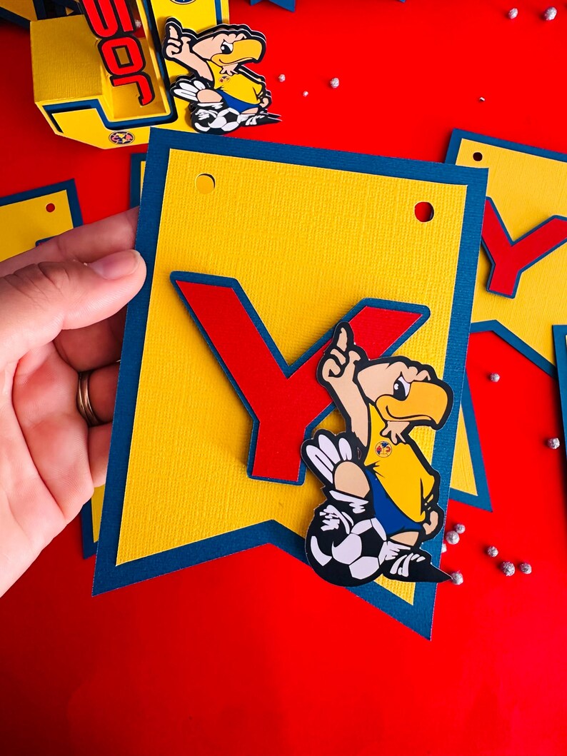 May include: A yellow and blue banner with the letter "Y" in red and a cartoon soccer player with a yellow jersey and blue shorts. The player is kicking a soccer ball.