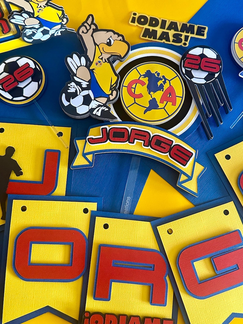 May include: A birthday banner with the name "JORGE" in red and blue letters on a yellow background. The banner also includes a blue and yellow soccer team logo with the letters "CA" and a soccer ball with the number "26" on it. The banner is decorated with a yellow and blue eagle mascot.