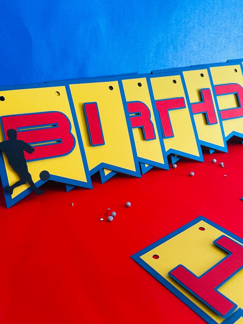 May include: A yellow and blue birthday banner with red letters spelling out "BIRTHDAY". A silhouette of a soccer player is on the left side of the banner.
