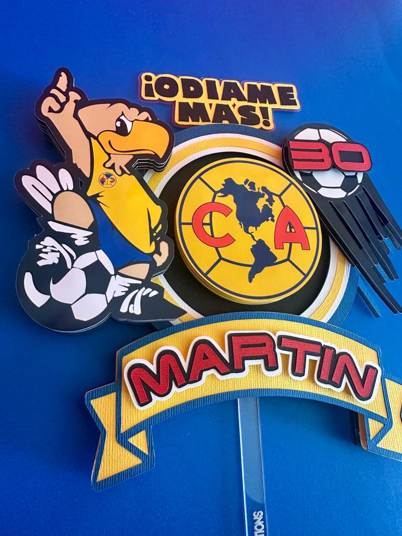 K&ouml;nnte beinhalten: Ein gelber und blauer Tortendekor mit einem Cartoon-Adler, der einen Fu&szlig;ball h&auml;lt. Der Dekor enth&auml;lt auch einen gelben und roten Kreis mit den Buchstaben "CA" und einen Fu&szlig;ball mit der Nummer "30" darauf. Der Dekor enth&auml;lt auch ein gelbes und blaues Banner mit dem Namen "MARTIN" darauf. Der Text "&iexcl;ODIAME MAS!" ist ebenfalls auf dem Dekor enthalten.