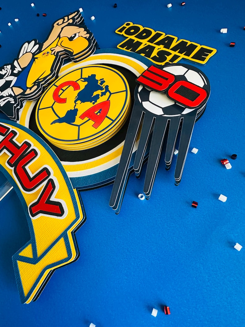 K&ouml;nnte beinhalten: Ein Set aus bunten Papierdekorationen f&uuml;r eine Geburtstagsparty. Die Dekorationen zeigen einen Fu&szlig;ball, ein gelbes und blaues Banner mit dem Wort "CHUY", einen gelben und blauen Kreis mit den Buchstaben "CA" und ein gelbes und schwarzes Banner mit dem Text "&iexcl;ODIAME MAS!"