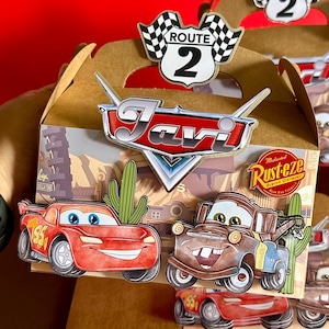 May include: A brown cardboard box with a handle, decorated with a Cars theme. The box features a red and white checkered flag with the words "Route 2" on it, a red and silver car logo with the name "Javi", and images of Lightning McQueen and Mater from the Cars movie. The box also includes a Rust-eze logo with the words "Medicated Bumper O'Shine" and "Near End Formula".
