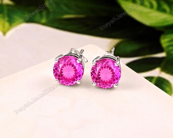 May include: A pair of stud earrings featuring round, faceted, vibrant pink gemstones set in polished silver-toned metal prongs. The earrings have a classic circular design with a brilliant cut that reflects light, showcasing a bright magenta hue.