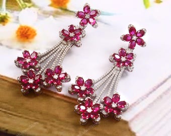 Puede incluir: Un par de pendientes colgantes plateados con múltiples racimos en forma de flor, engastados con piedras de color fucsia intenso en talla marquesa y pequeñas piedras claras. El diseño incluye tallos metálicos con pavé que unen las flores.