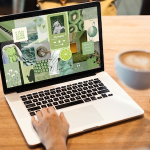 May include: A laptop computer with a green and white collage on the screen. The collage features images of plants, animals, and other objects. The laptop is sitting on a wooden table with a cup of coffee and a saucer next to it.