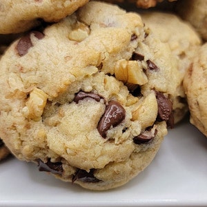 May include: Close-up of a golden brown cookie with chocolate chips and chopped walnuts. The cookie is soft and chewy, with a slightly crispy edge.