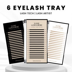 以下が含まれることがあります： 「6 EYELASH TRAY」と「LASH TECH | LASH ARTIST」の文字が入った、黒、ベージュ、ゴールドの3つのまつげエクステトレイ。各トレイにはまつげ配置用のセクションがあり、「NAME GOES HERE LUXURY LASH SALON」の文字が入っています。
