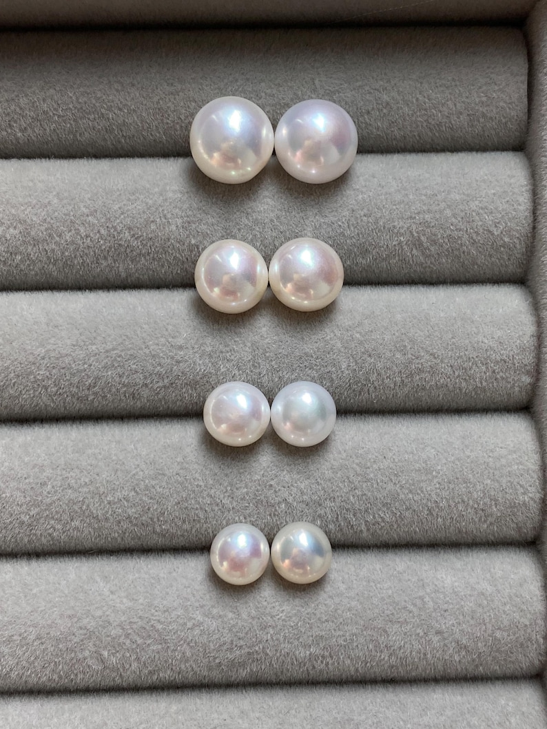 Pode incluir: Quatro pares de p&eacute;rolas redondas, brancas e lustrosas dispostas numa coluna vertical. Cada par consiste em duas p&eacute;rolas esf&eacute;ricas id&ecirc;nticas com uma superf&iacute;cie lisa e iridescente, exibindo subtis tons rosados e azulados sob a luz.