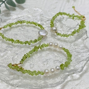 Peut inclure: Trois bracelets délicats composés de pépites de péridot et de perles d'eau douce. Les bracelets sont dans des tons de vert et de blanc, avec des fermoirs dorés. Les bijoux sont présentés sur une surface claire et texturée.