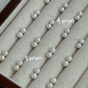 Peut inclure: Plusieurs paires de boucles d'oreilles &agrave; clous en perles blanches, certaines de 4 mm et d'autres de 5 mm de diam&egrave;tre, sont pr&eacute;sent&eacute;es dans un &eacute;crin &agrave; bijoux doubl&eacute; de tissu beige. Le texte "LYS HANDMADE SHOP" est visible en haut.