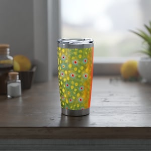 May include: A stainless steel travel tumbler with a colorful trout pattern. The tumbler has a lid and is designed for hot or cold beverages.