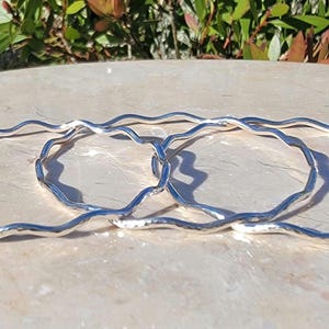 May include: Three silver bangles with a wavy, textured design. The bangles are stacked on top of each other.