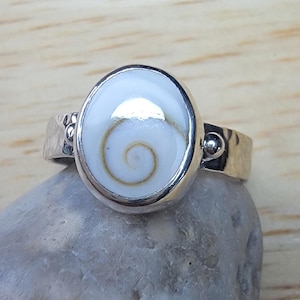 May include: A silver ring with a white oval shell inlay featuring a brown spiral pattern.
