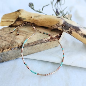 May include: A delicate beaded bracelet with a sliding knot closure. The bracelet features small, turquoise, beige, and copper beads.