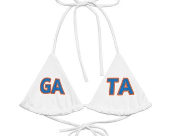 May include: White bikini top with the letters "GA" and "TA" in blue with orange trim. The top has tie closures at the neck and back. The bikini top is a triangle style.