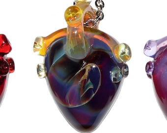 Puede incluir: Cuatro colgantes de corazón de cristal en tonos rojo, morado e iridiscente, cada uno suspendido de una cadena plateada. Los colgantes presentan detalles anatómicos, mostrando un diseño artístico único. Ideal para quienes aprecian la joyería única.
